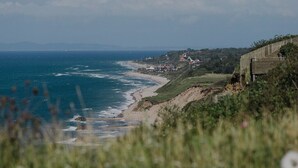 A coastal landscape with a beach, houses, and a wooden fence. - Havgaarden Badehotel (Vejby)