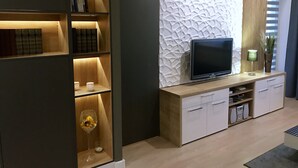 Ett modernt vardagsrum med en platt-TV, hyllor i trä och en dekorativ väggpanel.