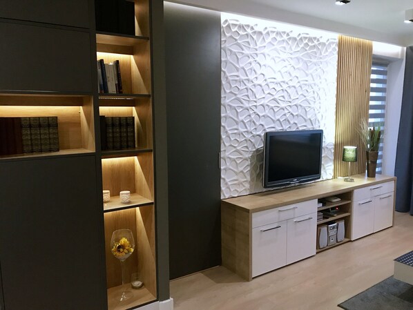 A modern living room with a flat-screen TV, wooden shelving, and a decorative wall panel. - 4UApart-Apartment suite Emporio (Swinoujscie)