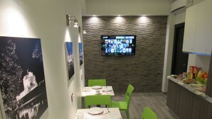 Ein Restaurant mit einer Steinwand, einem Bildschirm, grünen Stühlen und einer Theke mit Speisen.