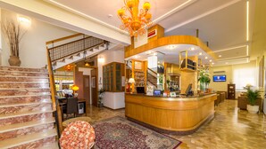 A hotel lobby with a reception desk, a staircase, and a large chandelier. - Hotel Touring (Jesolo)