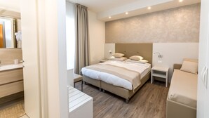 A modern hotel room with a large bed, bedside tables, a small desk, and a bathroom visible through an open door. - Hotel Touring (Jesolo)