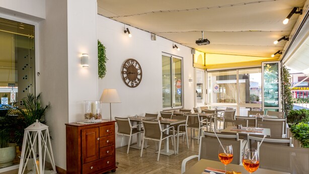 A restaurant with wooden furniture, a clock on the wall, and a view of the street outside. - Hotel Touring (Jesolo)