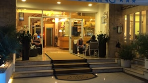 A hotel entrance with a reception desk, a waiting area with chairs, and a staircase leading to the lobby. - Hotel Touring (Jesolo)
