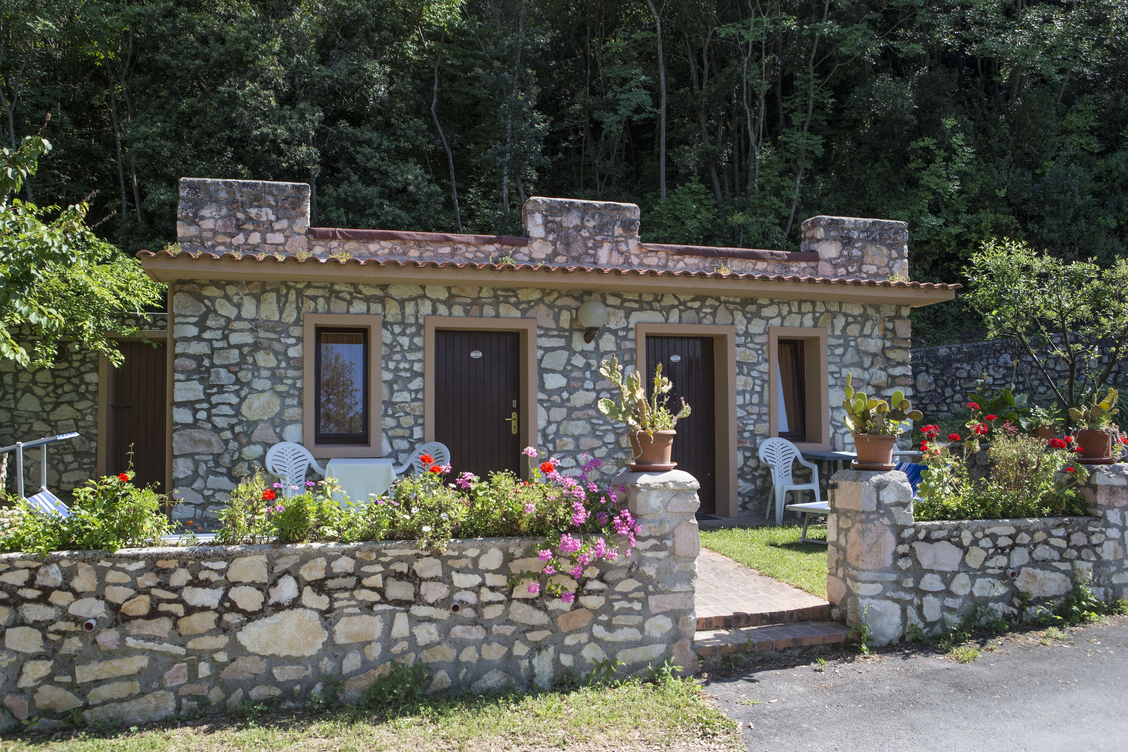 Un edificio de piedra con techo de tejas, dos puertas y un pequeño porche con plantas y flores en macetas.