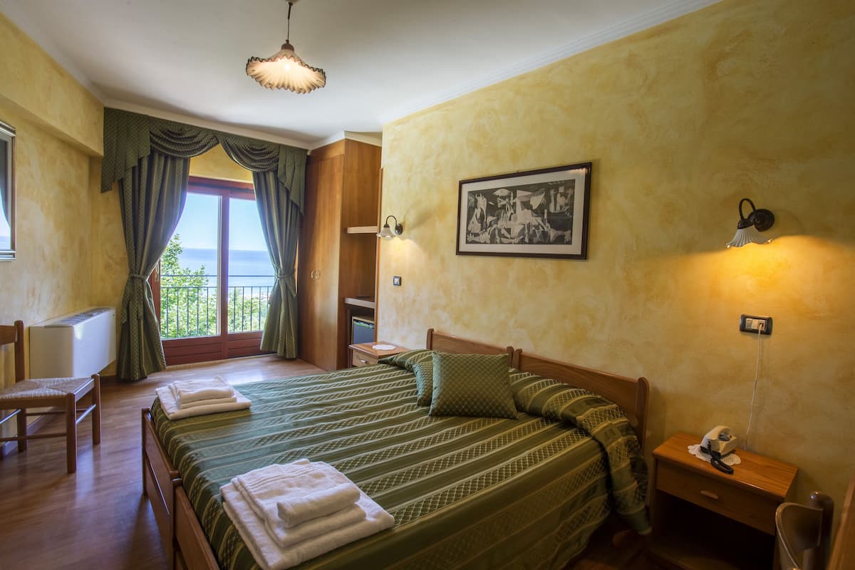 A bedroom with a large bed, a chair, a desk, and a window with curtains.