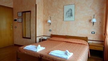 Una camera d'albergo con un letto di legno, un comodino, uno specchio e una lampada a parete.