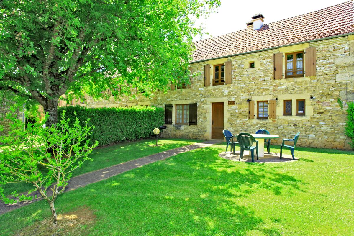 Un bâtiment en pierre doté d’un patio avec jardin, d’un petit arbre et d’une haie.