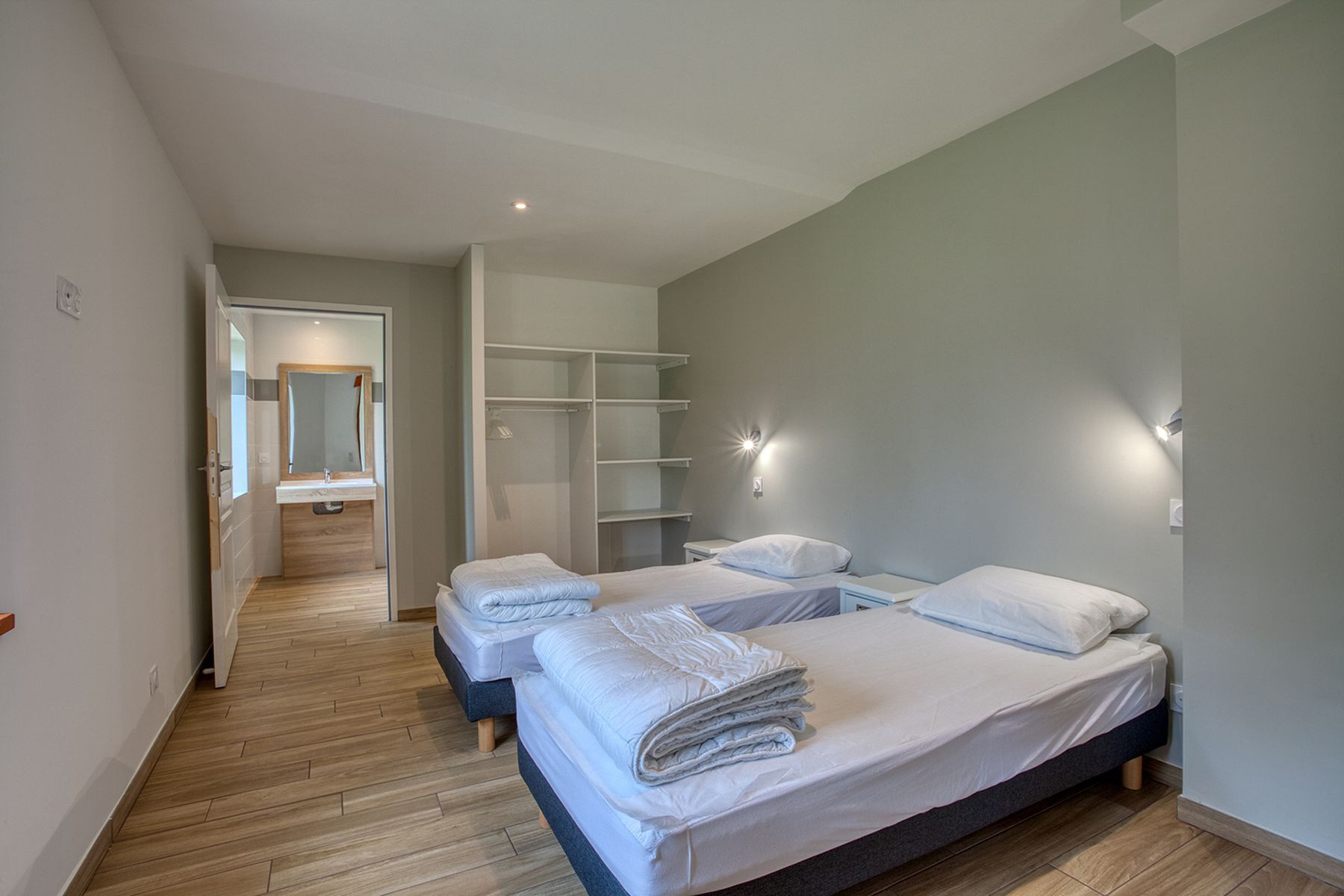 Ein modernes Schlafzimmer mit zwei Betten, einem begehbaren Kleiderschrank und einem Badezimmer mit Spiegel.