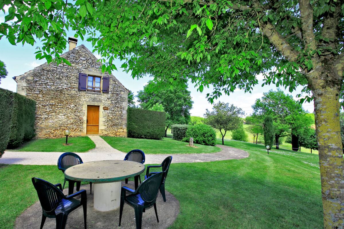 Une maison en pierre avec une porte en bois, une table ronde entourée de chaises et une pelouse bien entretenue.
