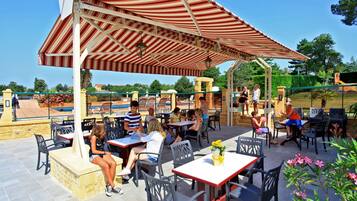 Relax in the shaded patio area with comfortable seating for all, surrounded by a landscaped pool and play area.