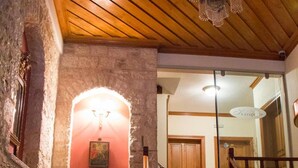 Una escalera de madera que conduce a un segundo piso, una pared de piedra con un cuadro enmarcado y una araña.