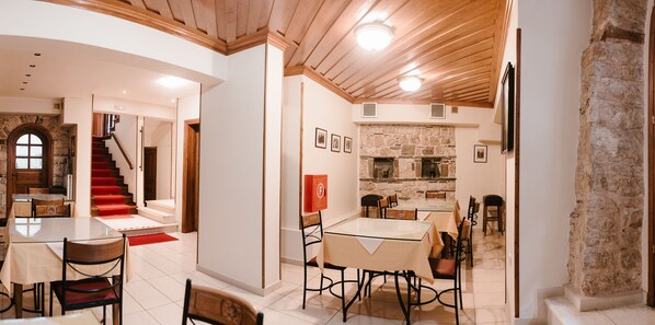 A spacious dining area with a stone fireplace, a staircase leading to an upper level, and a modern kitchen visible through an open door. - Kentrikon Hotel (Ioannina)