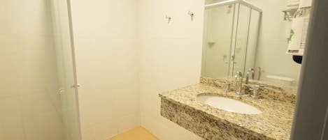 Un baño con lavamanos de granito, cabina de ducha de vidrio y espejo sobre el lavamanos.