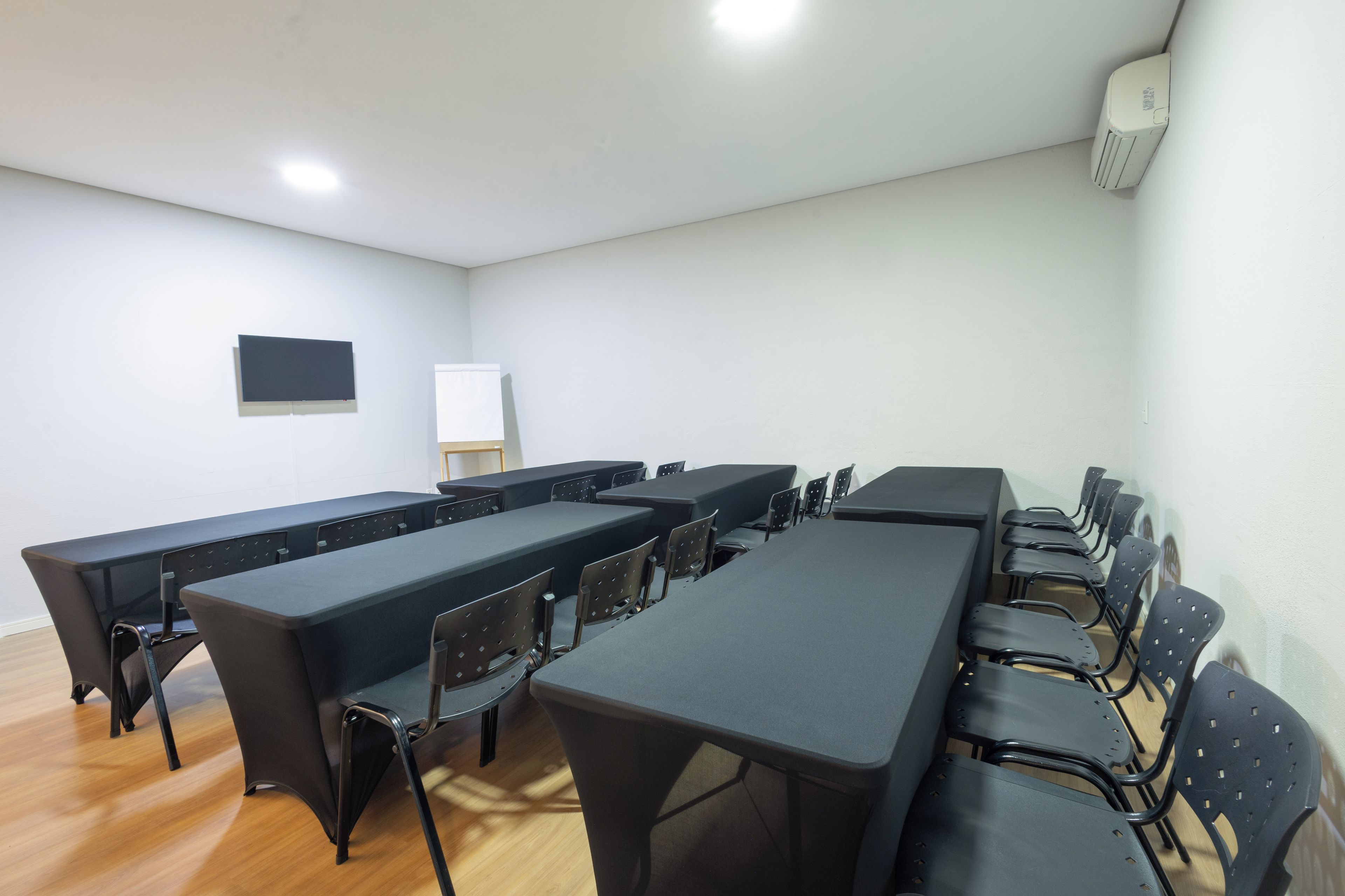 Un salón de conferencias con varias mesas y sillas, una pizarra y un equipo de aire acondicionado en la pared.