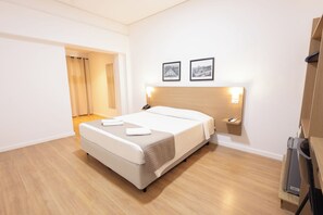 A hotel room with a bed, a bedside table, a wall-mounted phone, and two framed pictures. - Transamerica Fit Jaú (Jau)