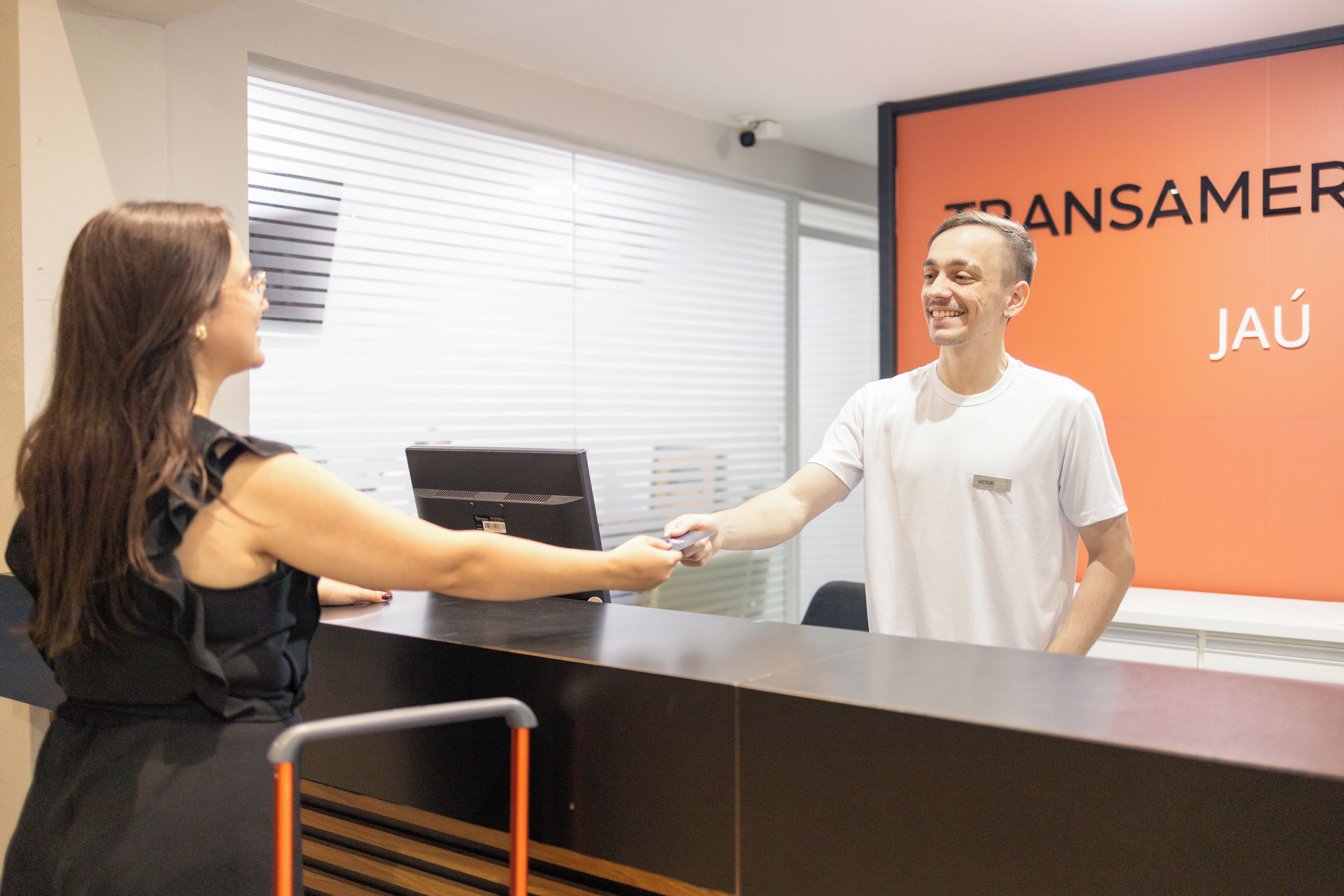 Uma área de recepção com placa, computador e janela com persianas.
