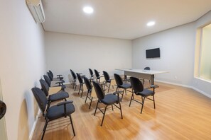 A conference room with a long table, multiple chairs, a flat-screen TV mounted on the wall, and wooden flooring. - Transamerica Fit Jaú (Jau)