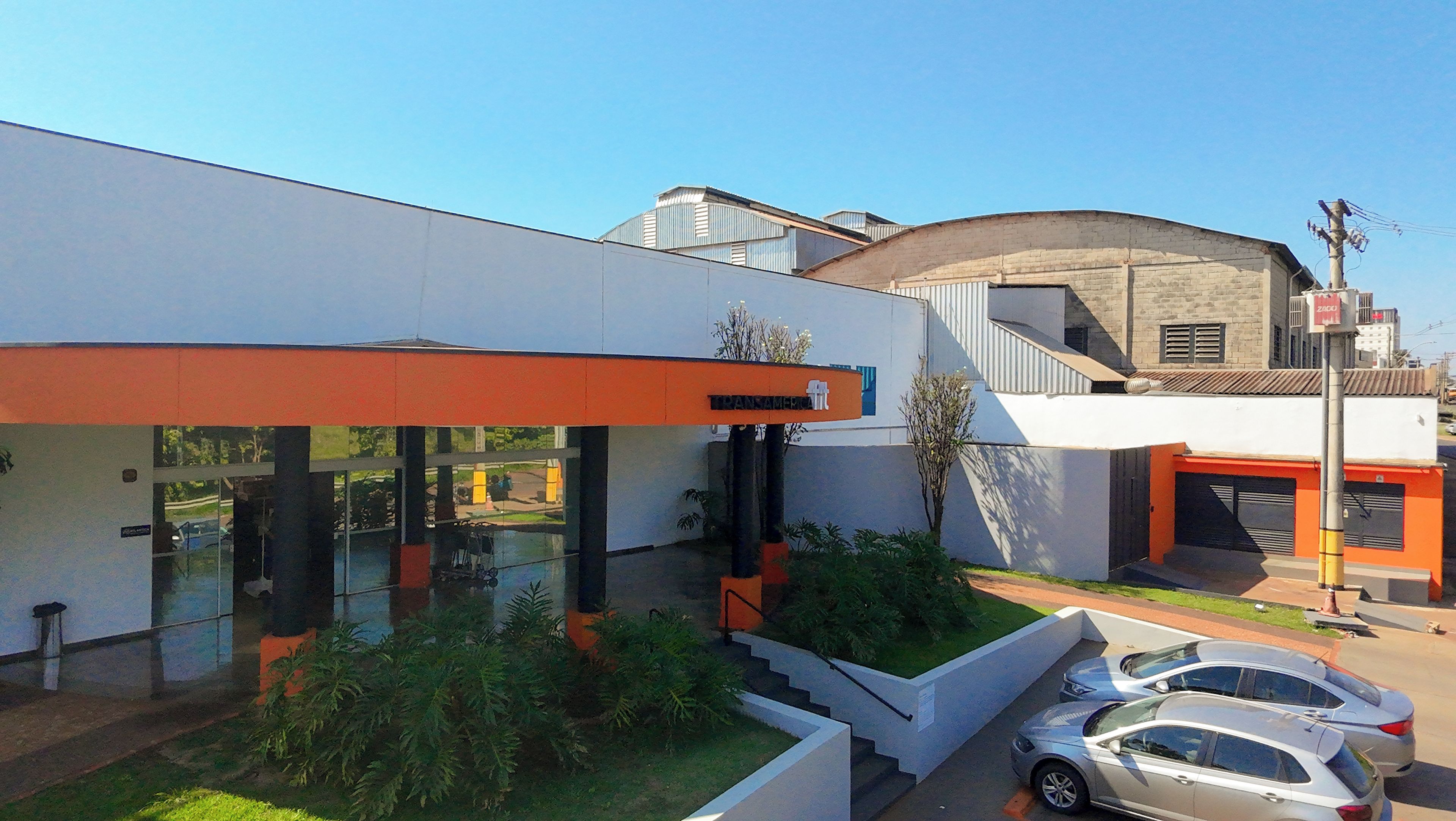 Un edificio moderno con techo plano, grandes ventanales y un estacionamiento con coches.