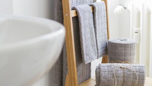 A bathroom with a wooden towel rack holding two towels and a rolled towel on a wooden table. - FeelinRome Bed & Breakfast (Rome)