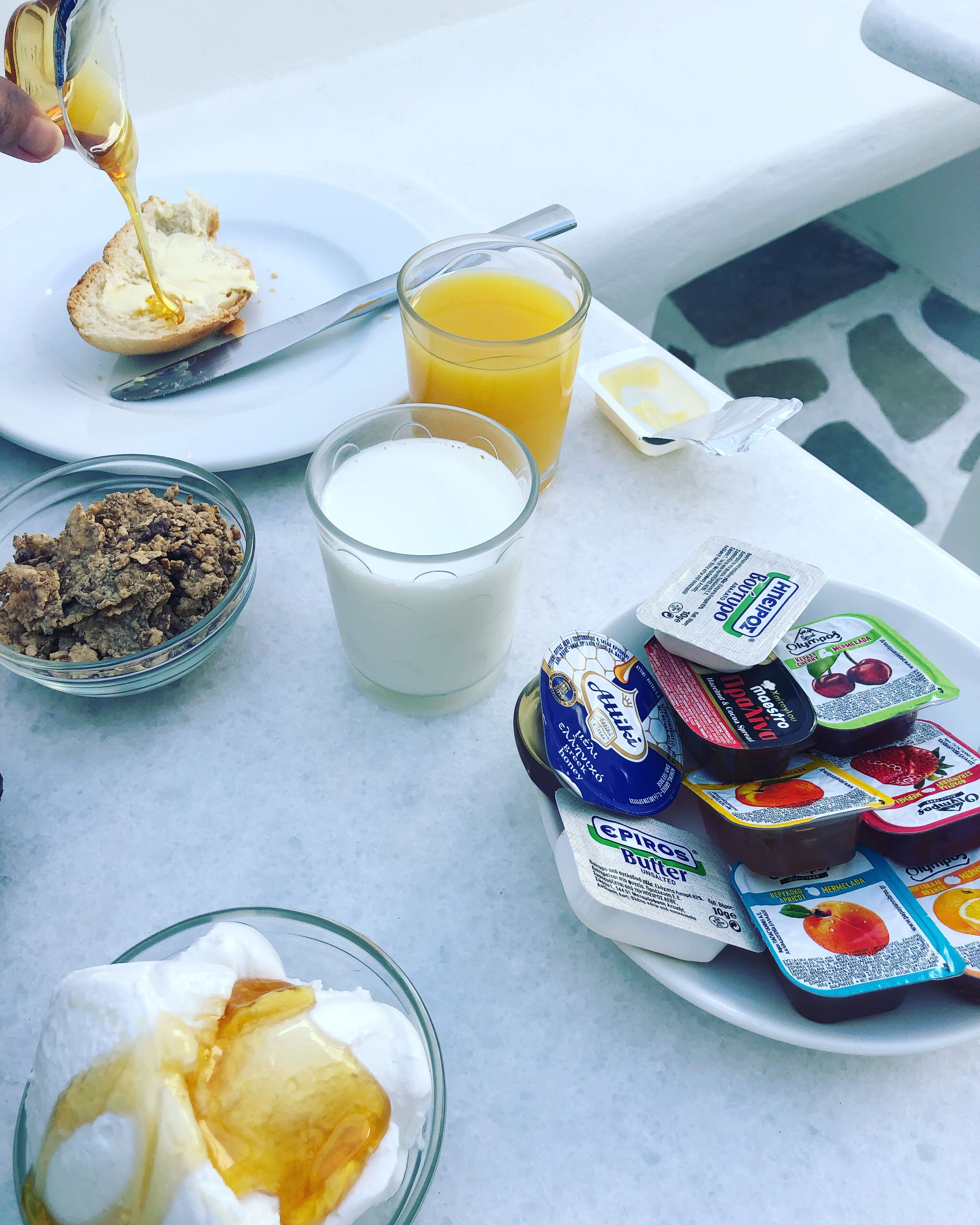 Une table de petit-déjeuner avec des tartines, du beurre, du lait, du jus d’orange et différents pots de yaourt.