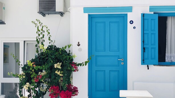 Un edificio blanco con puerta azul, plantas en macetas y piso de baldosas.