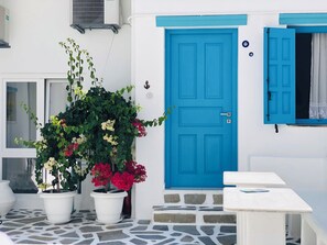 A white building with a blue door, potted plants, and a tiled floor. - Taki's Guests (Naxos)