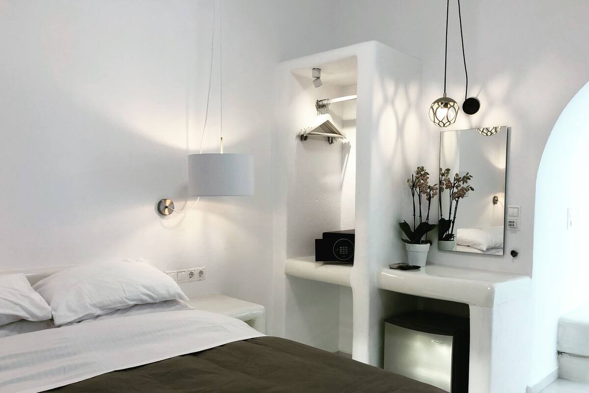 A modern hotel room with a bed, a vanity with a mirror, a small plant, and a wall-mounted heater.