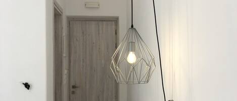 A hallway with a wooden door, a hanging pendant light, and a bed with white bedding.