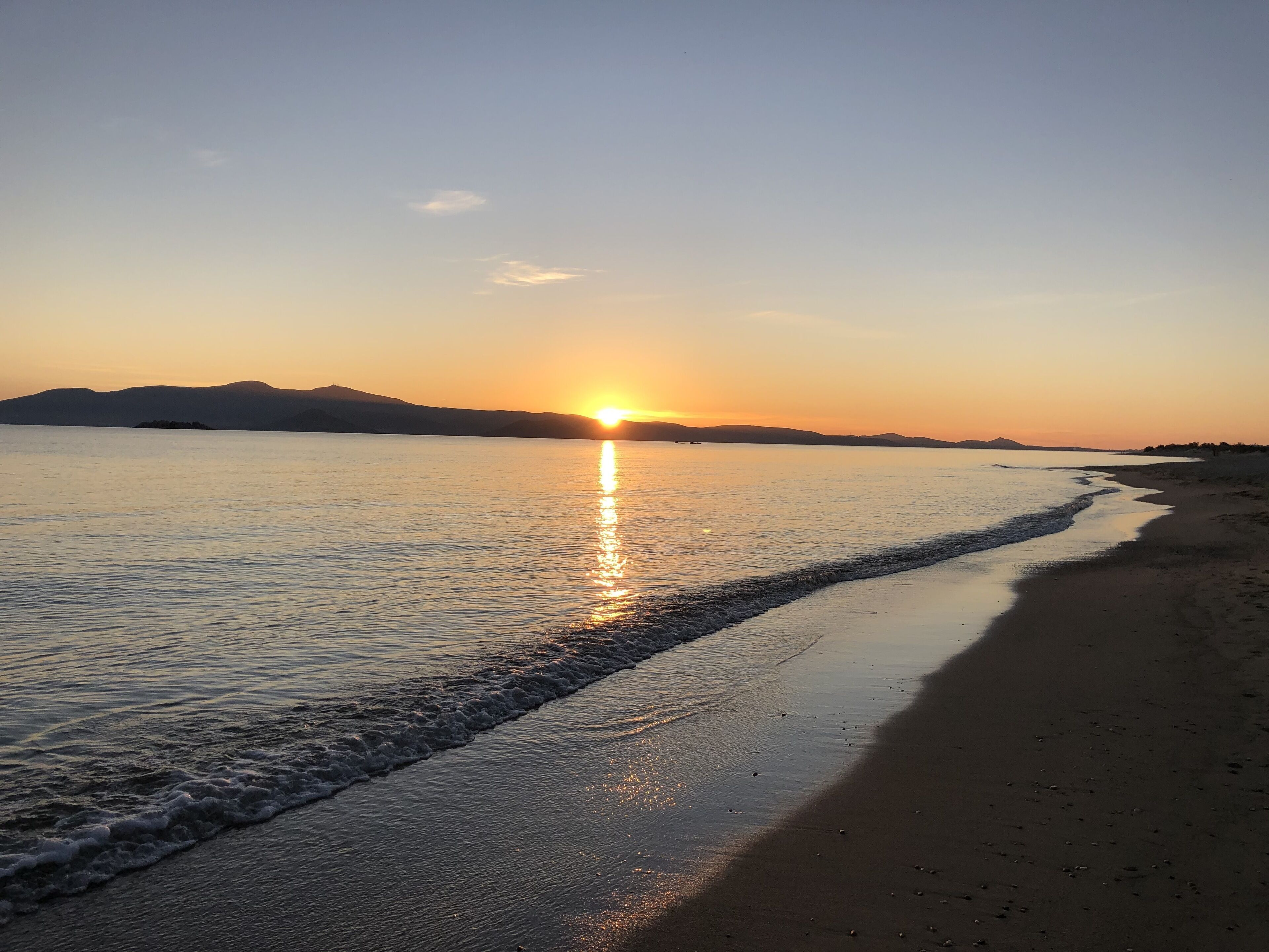 Una playa al atardecer con aguas tranquilas que reflejan el cielo.