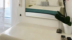 Habitación de hotel con un espejo grande, una cama con ropa blanca, un plaid verde, una orquídea en maceta y una lámpara colgante.