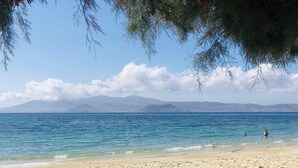Una playa con agua azul cristalina, orilla de arena y montañas a lo lejos.