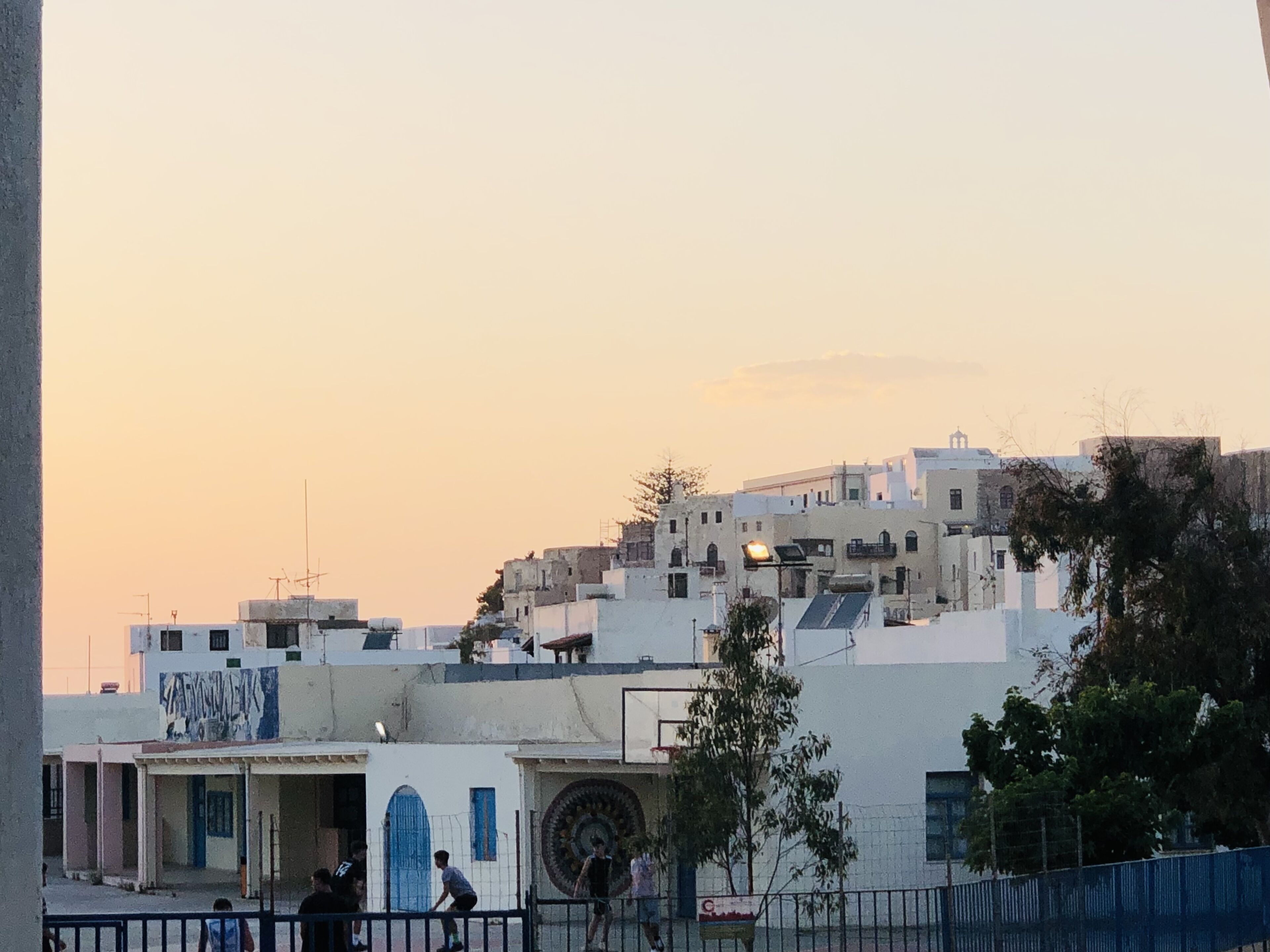 A residential area with buildings, a basketball court, and a few people.