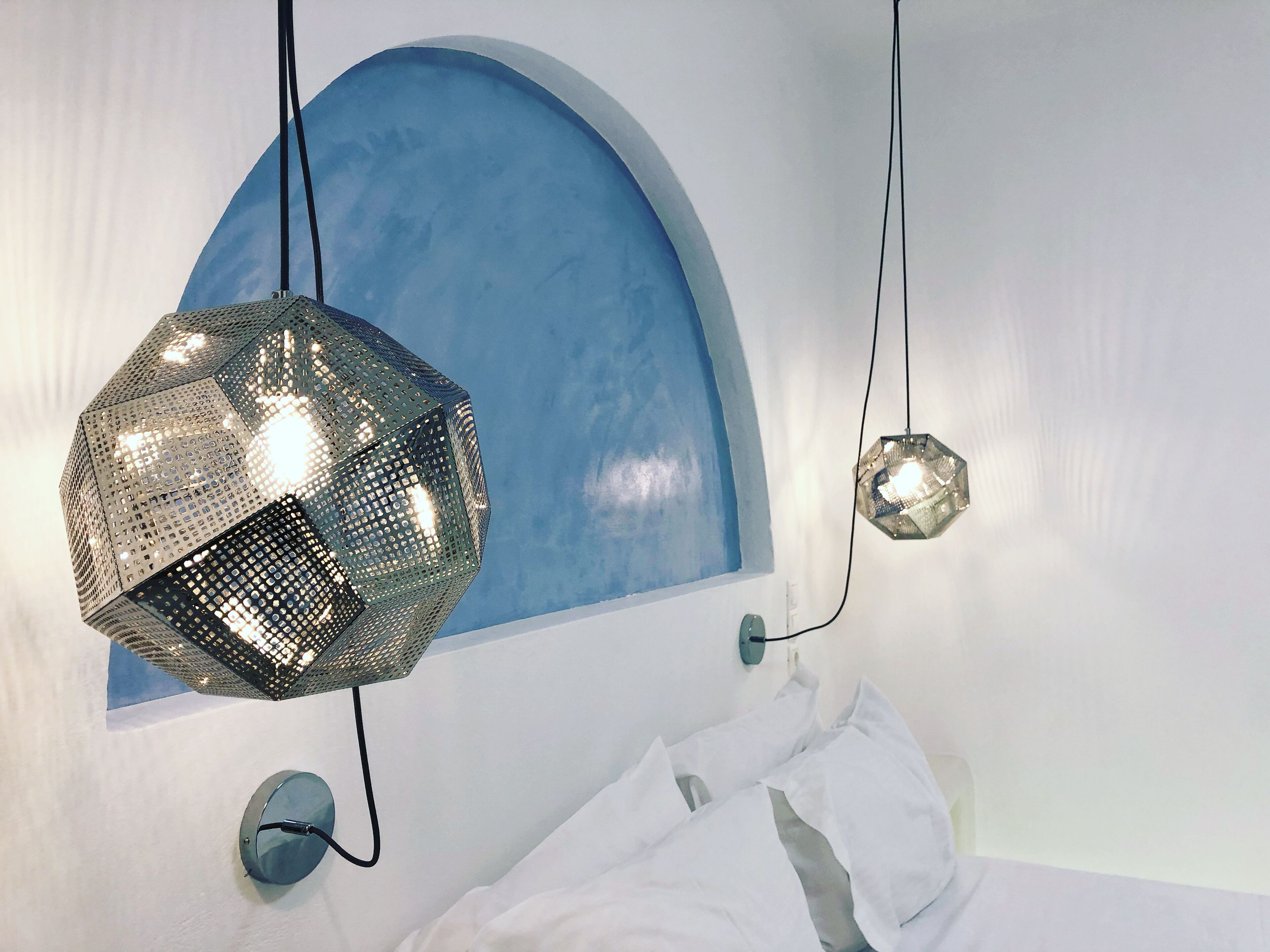 A bedroom with a bed, a blue arched wall, and two hanging lights.