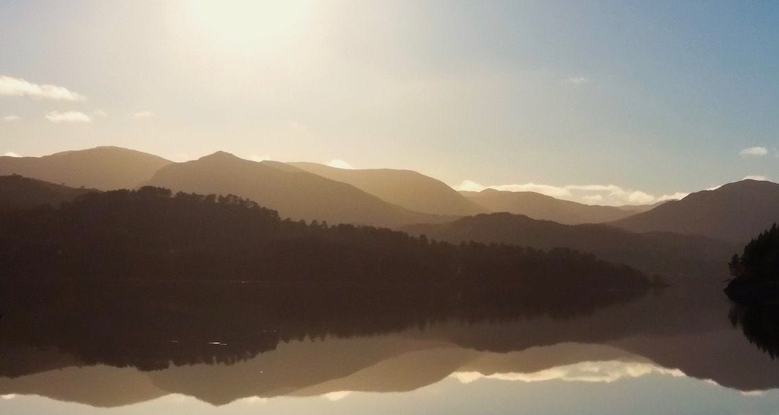 A calm lake reflecting mountains and a clear sky.