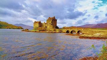 A historic castle by a river with a bridge leading to it.
