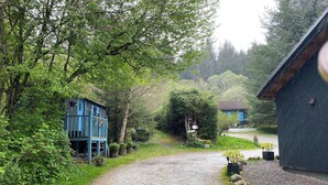A gravel path leading to a blue building with a balcony, surrounded by greenery and trees. - Loch Ness Highland Cottages (Inverness)