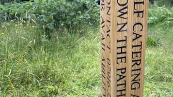 A wooden sign with the text "SELF CATERING ACCOMMODATION" and "CONTACT 0791 335 033" against a natural backdrop.