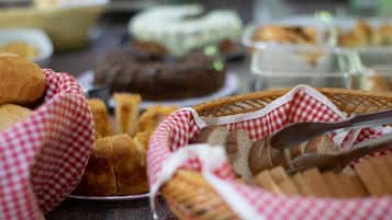 Una mesa de buffet con diversos productos de panadería y una cesta con panecillos.
