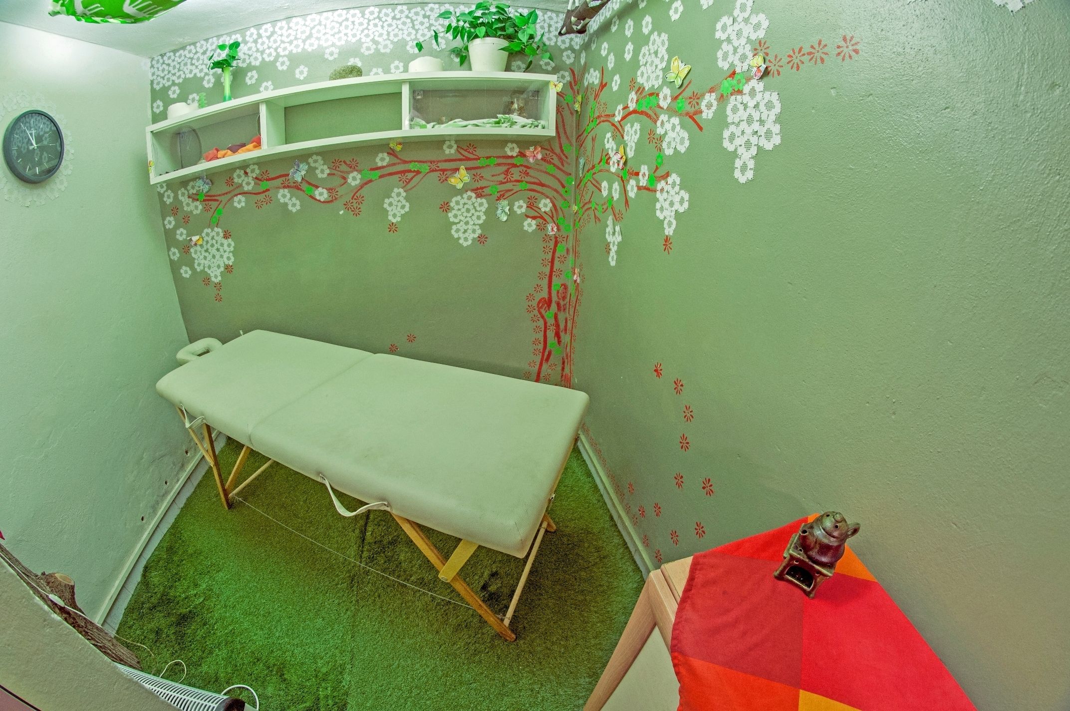 A small room with a single bed, a shelf with decorative items, and a clock on the wall.