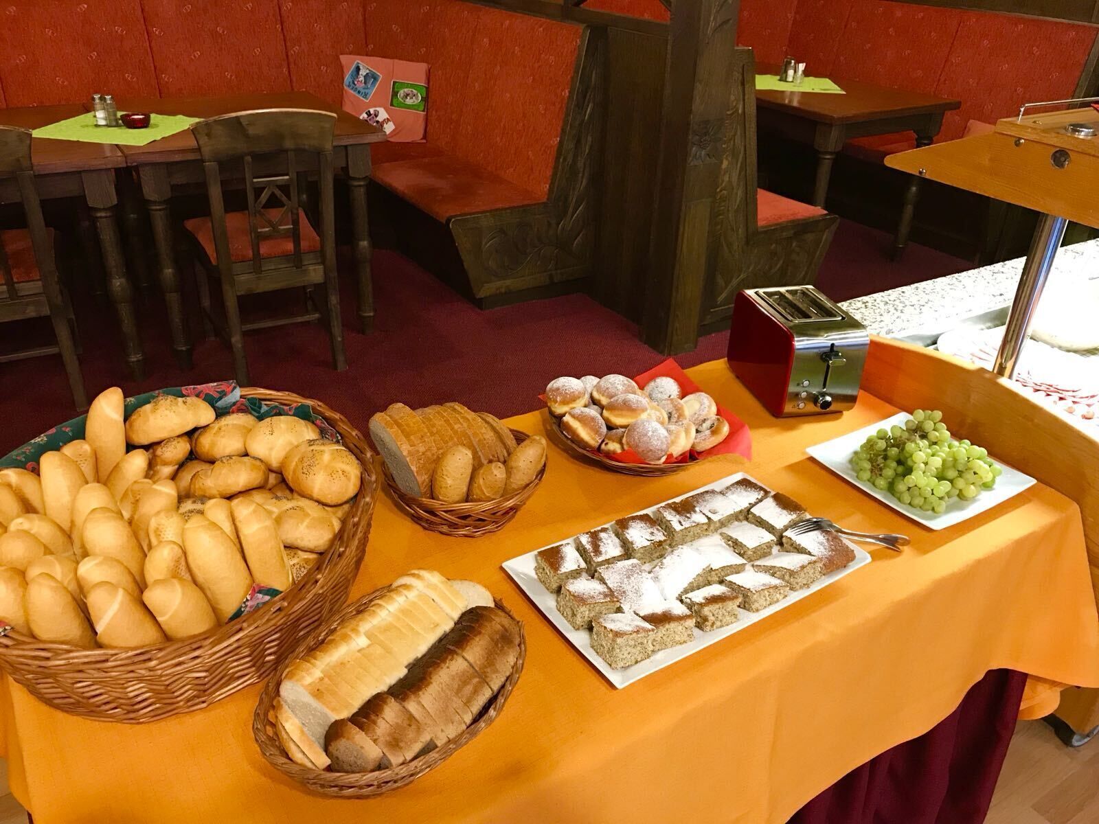 A buffet table with various breads, pastries, and a plate of grapes.