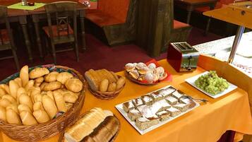 A buffet table with various breads, pastries, and a plate of grapes.