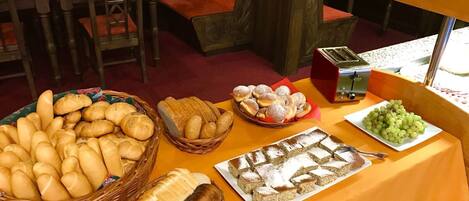 Una mesa de buffet con panes, pasteles y una fuente de uvas.