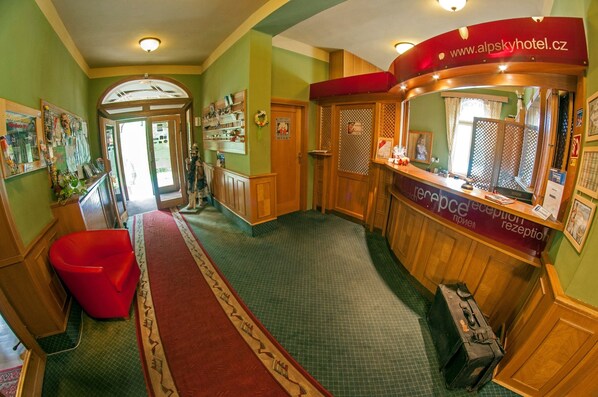 A reception area with a wooden reception desk, a red chair, and a check-in counter. - Alpský hotel (Spindleruv Mlyn)