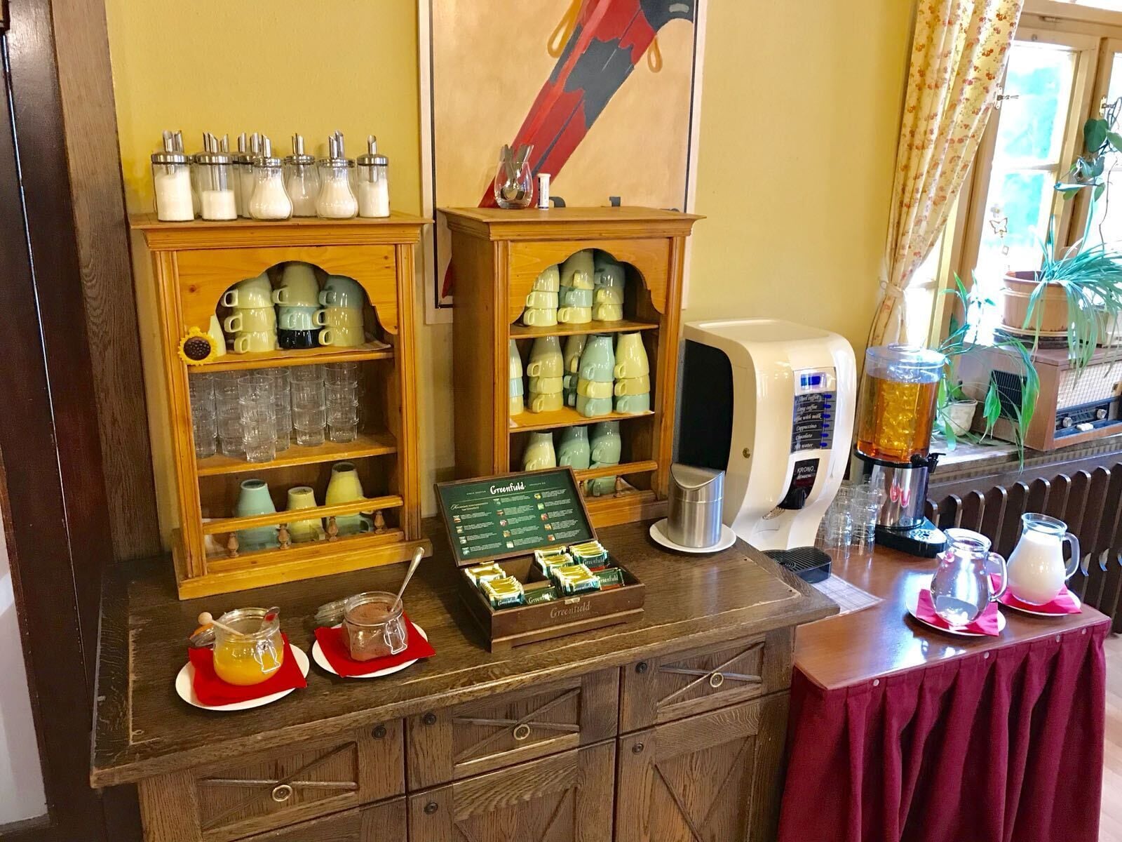 Una estación de café con una máquina de café, tazas y una exhibición de productos de Greenfield.