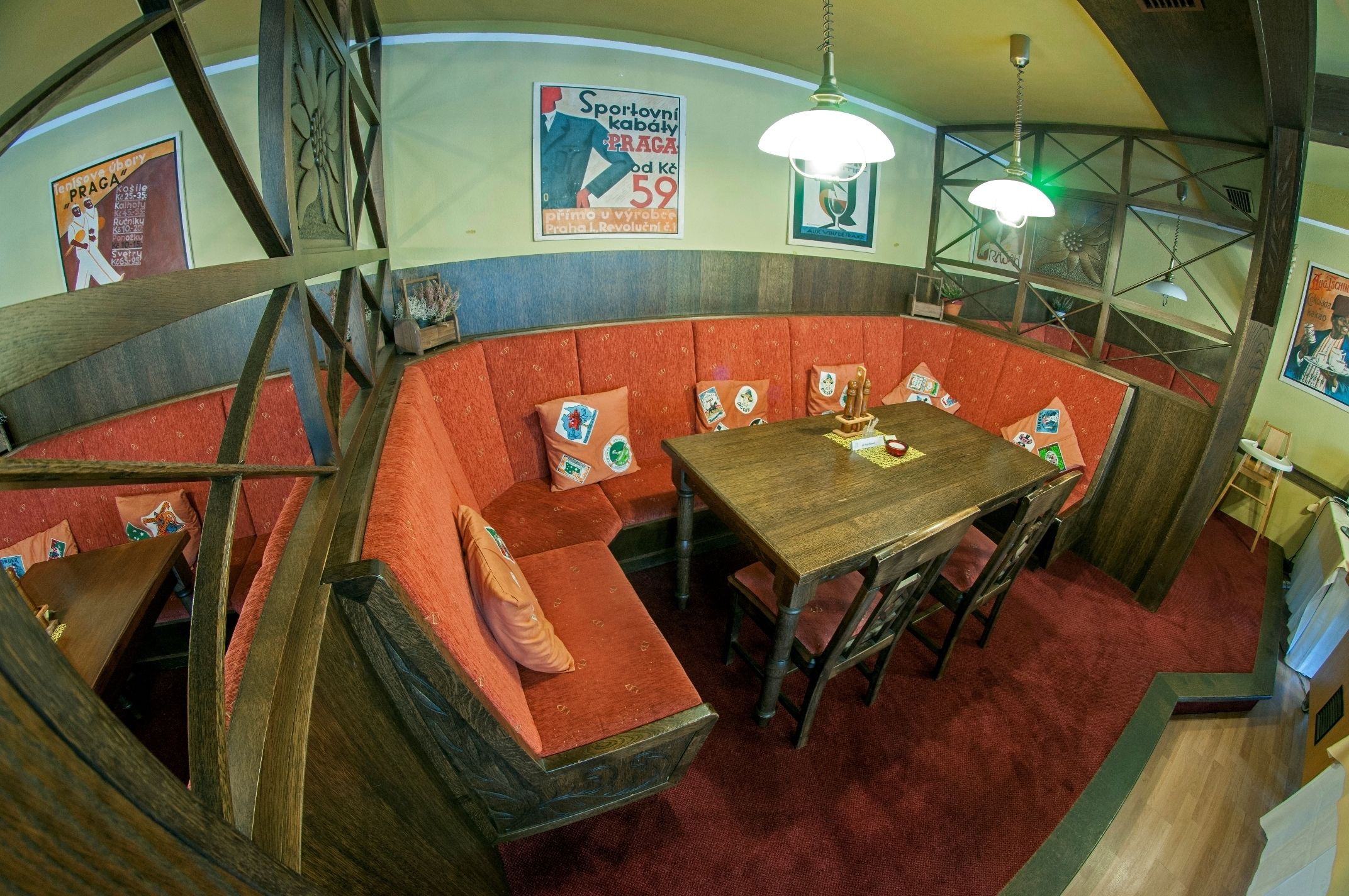 Une pièce chaleureuse, décorée dans un style vintage, avec une table et des bancs en bois, des sièges recouverts d’un tissu rouge et un escalier.