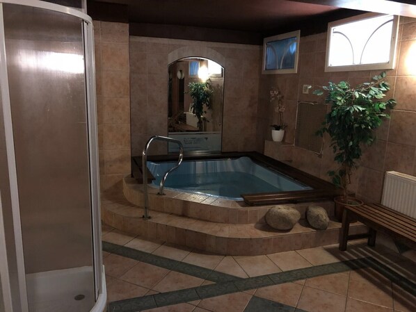 A bathroom with a bathtub, a shower, and a mirror. There is a potted plant and a bench.