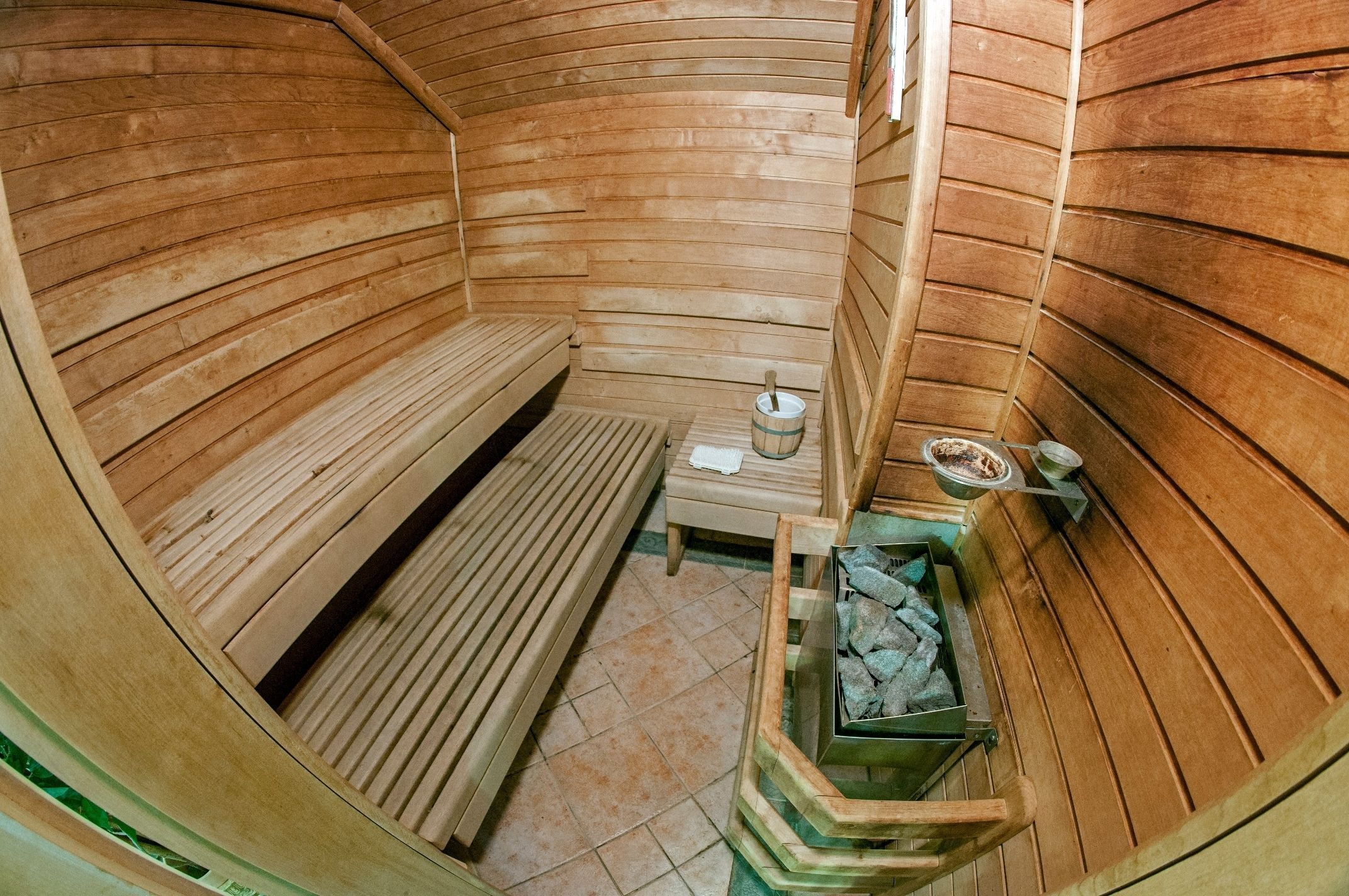 A wooden sauna with benches, a small table, and a container of stones.