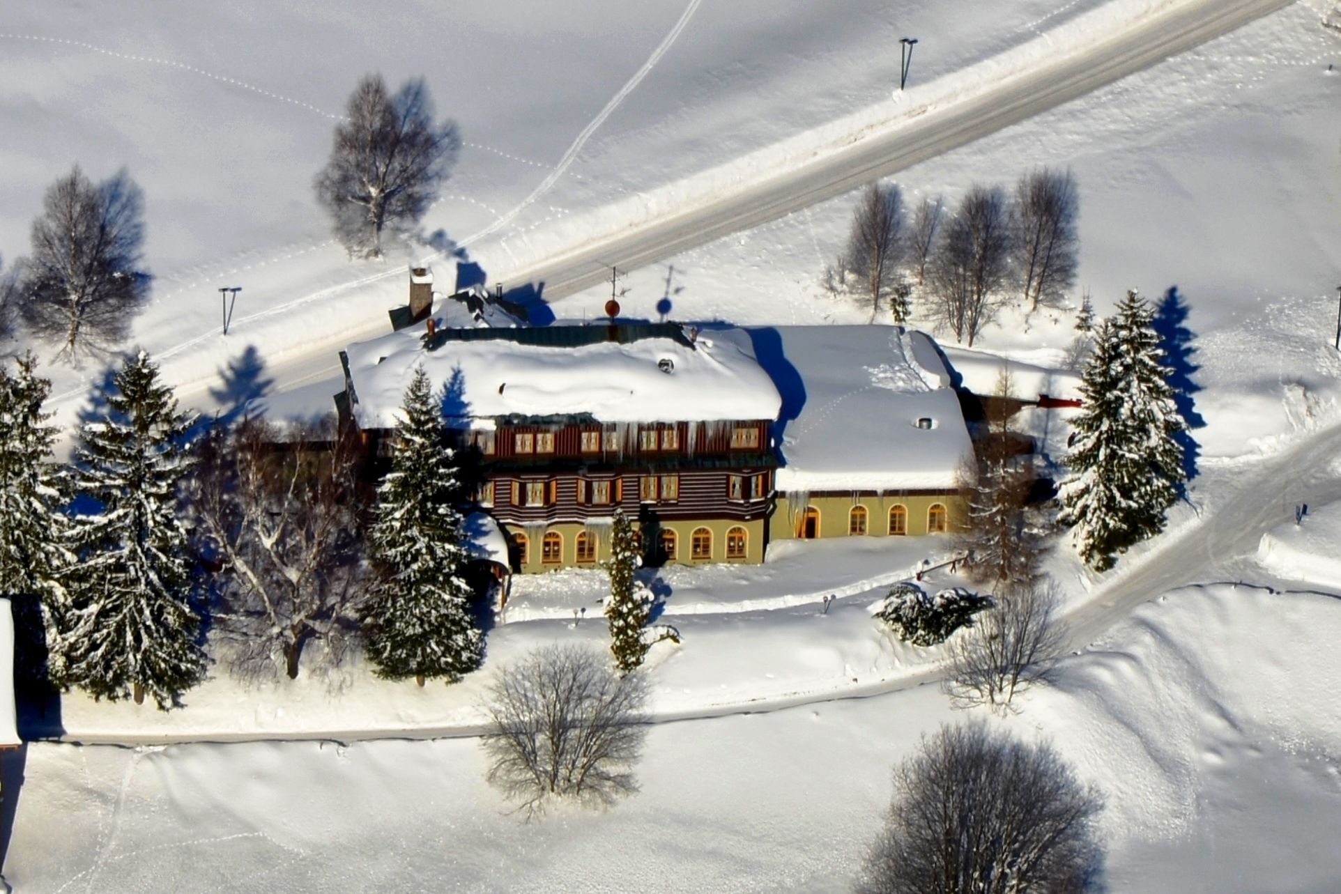 Un edificio grande de varios pisos con techo nevado, rodeado de árboles cubiertos de nieve y una pista de esquí.