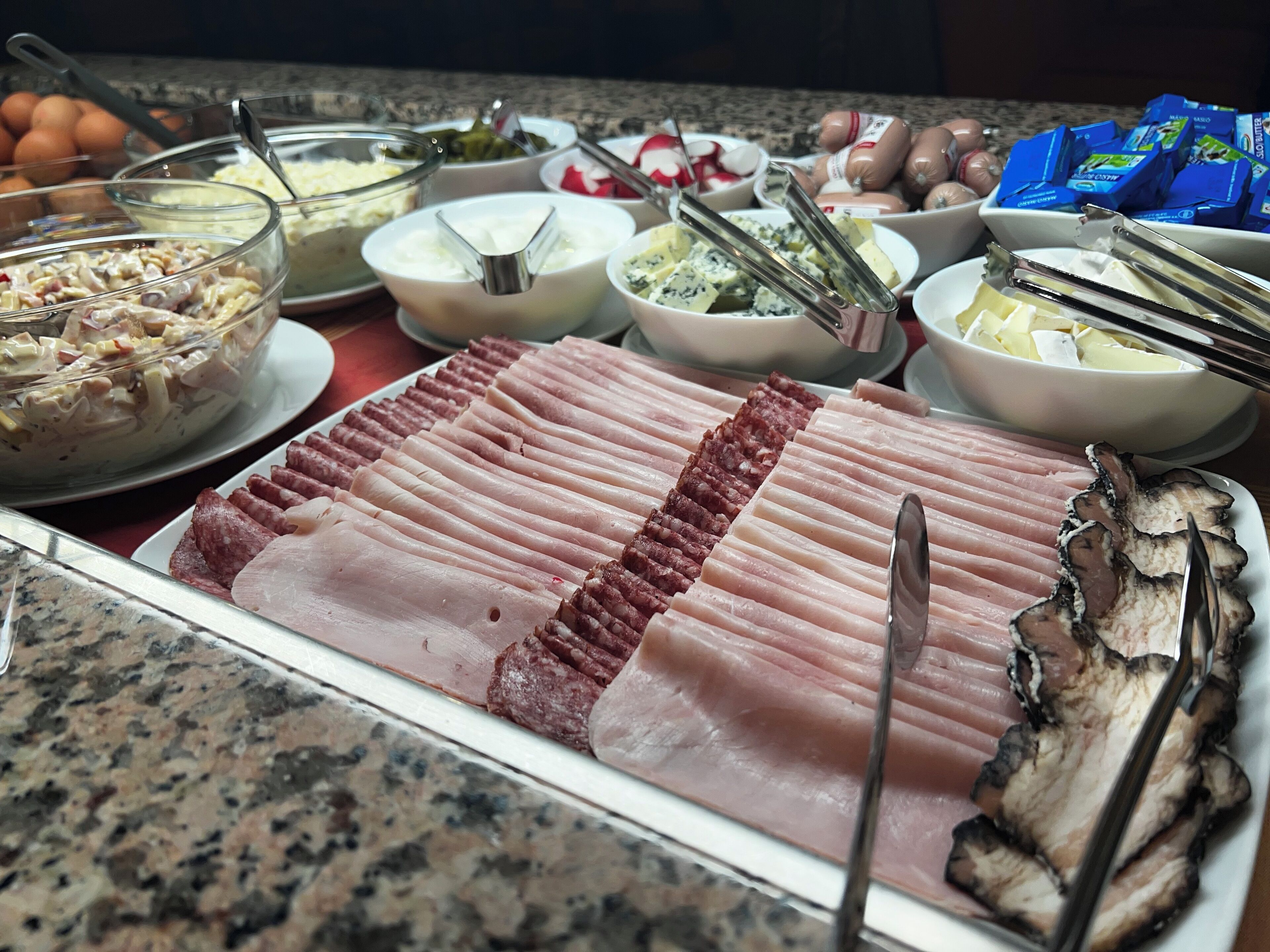 Un bufé con diversas opciones de comida, incluyendo carnes cortadas, quesos y otros platos.